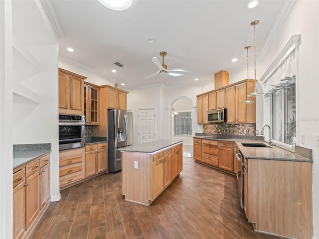 kitchen with sink, ornamental molding, appliances with stainless steel finishes, a kitchen island, and dark hardwood / wood-style flooring