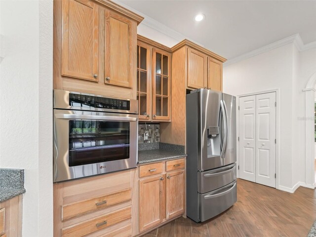 kitchen featuring crown molding, decorative backsplash, dark stone countertops, appliances with stainless steel finishes, and wood-type flooring