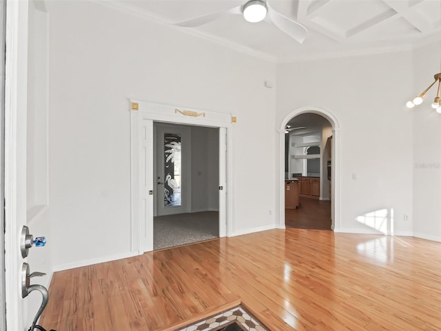 empty room featuring ceiling fan, wood-type flooring, ornamental molding, and a towering ceiling