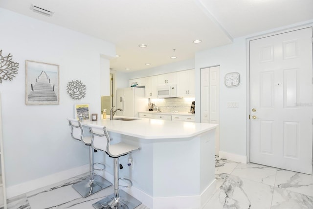 kitchen with kitchen peninsula, white cabinetry, light tile flooring, white appliances, and a breakfast bar area