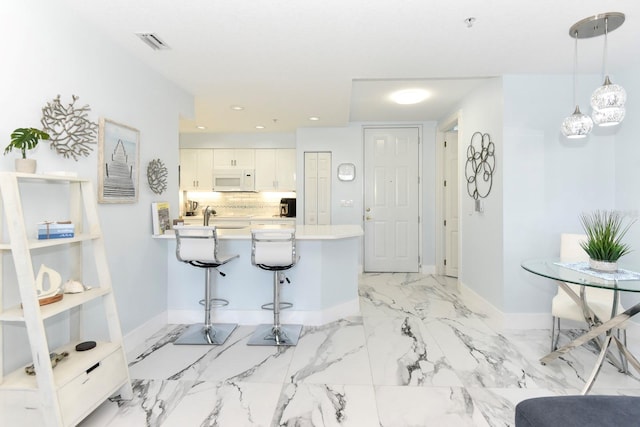 kitchen with hanging light fixtures, backsplash, a kitchen breakfast bar, light tile floors, and white cabinets