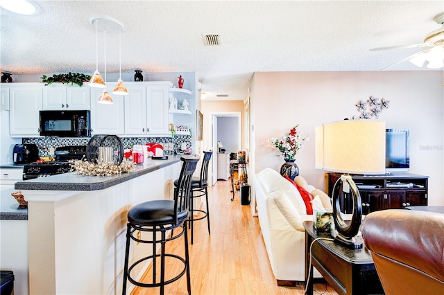 kitchen with ceiling fan, stove, a kitchen breakfast bar, white cabinets, and light hardwood / wood-style floors