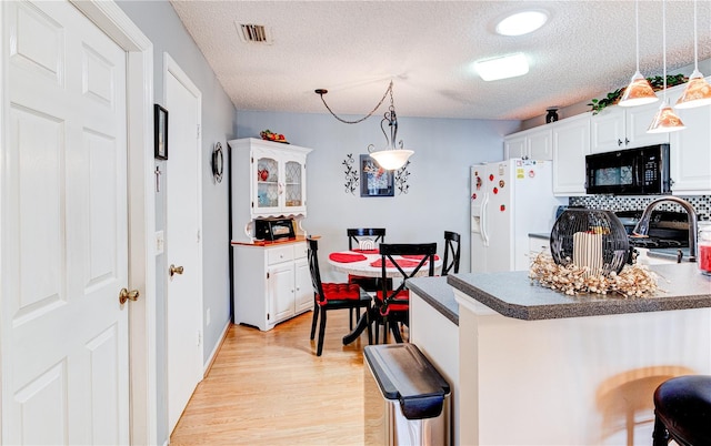 kitchen with a breakfast bar area, pendant lighting, white fridge with ice dispenser, and white cabinets