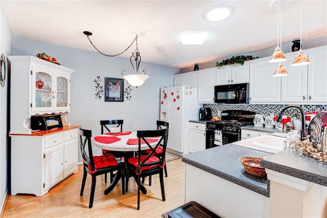 kitchen with white cabinets, light wood-type flooring, decorative light fixtures, and black appliances