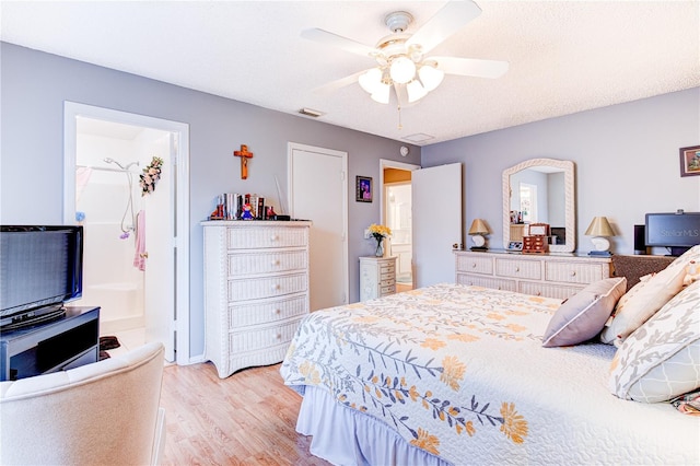 bedroom with a textured ceiling, ensuite bath, ceiling fan, and light wood-type flooring