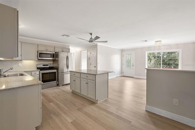 kitchen with sink, backsplash, a center island, light stone counters, and stainless steel appliances