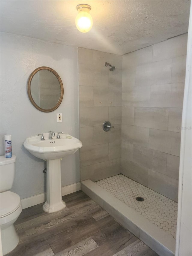 bathroom with tiled shower, wood-type flooring, and toilet