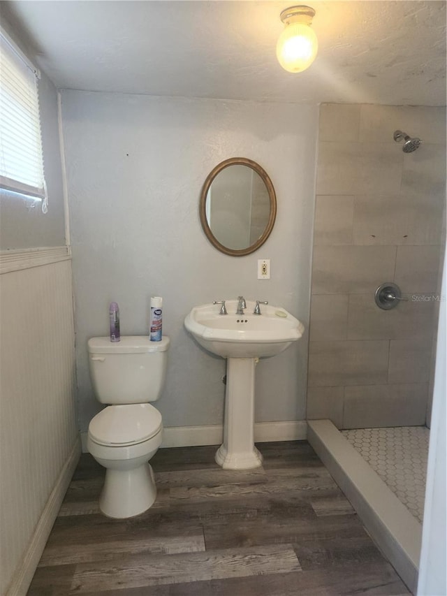 bathroom with toilet, a tile shower, and hardwood / wood-style flooring