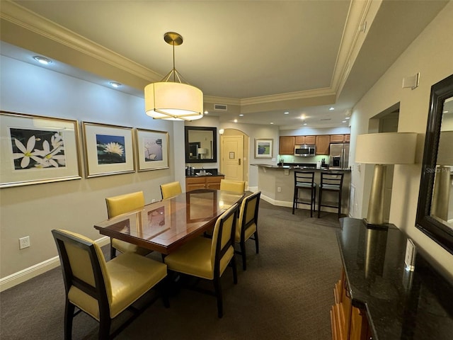 dining area with a tray ceiling, crown molding, and dark colored carpet