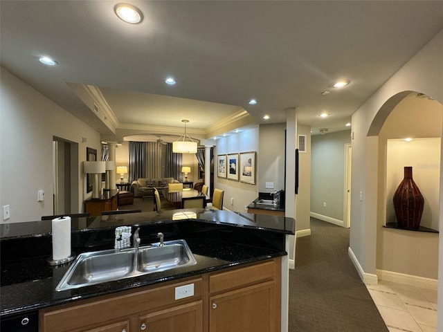 kitchen with decorative light fixtures, dark stone counters, ornamental molding, light carpet, and sink