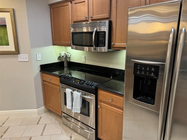 kitchen featuring light tile floors, dark stone countertops, and stainless steel appliances