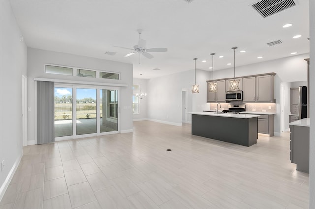 kitchen featuring ceiling fan with notable chandelier, a kitchen island with sink, light tile patterned flooring, backsplash, and stainless steel appliances