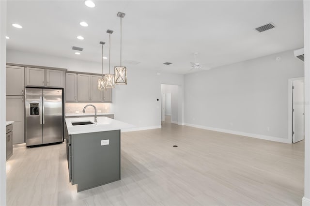 kitchen with decorative backsplash, a kitchen island with sink, stainless steel refrigerator with ice dispenser, gray cabinetry, and sink