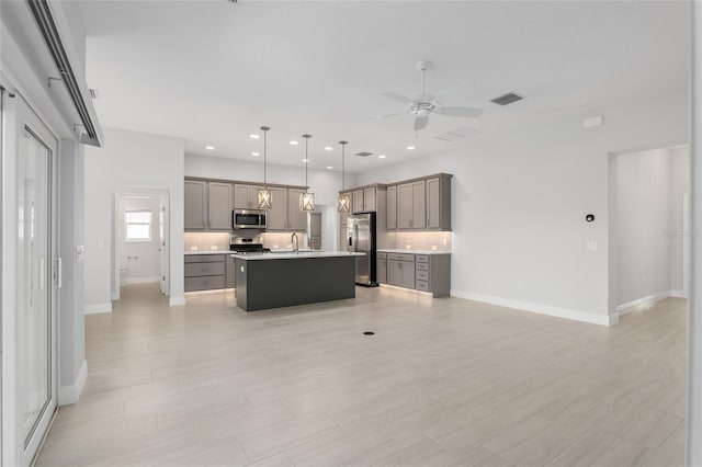 kitchen with appliances with stainless steel finishes, an island with sink, ceiling fan, gray cabinetry, and decorative light fixtures