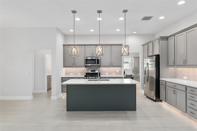 kitchen with gray cabinetry, backsplash, an island with sink, and stainless steel appliances