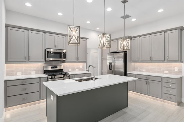 kitchen with stainless steel appliances, decorative backsplash, an island with sink, sink, and gray cabinetry