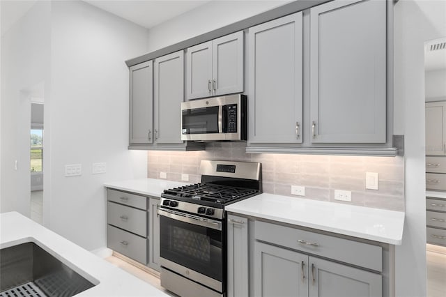 kitchen with tasteful backsplash, light hardwood / wood-style flooring, stainless steel appliances, and gray cabinetry