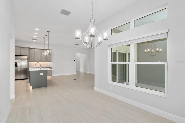 kitchen featuring a kitchen island with sink, hanging light fixtures, sink, decorative backsplash, and stainless steel refrigerator with ice dispenser