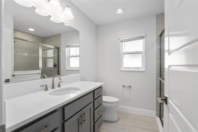 bathroom with toilet, a shower with door, vanity, and a healthy amount of sunlight