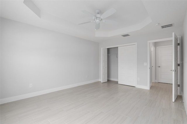 unfurnished bedroom with ceiling fan, a tray ceiling, and a closet