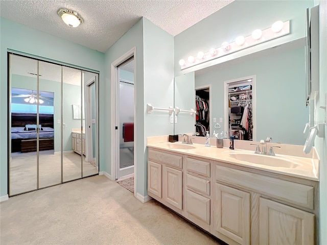 bathroom featuring large vanity, dual sinks, ceiling fan, and a textured ceiling