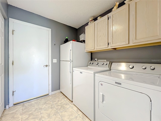 clothes washing area with a textured ceiling, separate washer and dryer, light tile floors, and cabinets