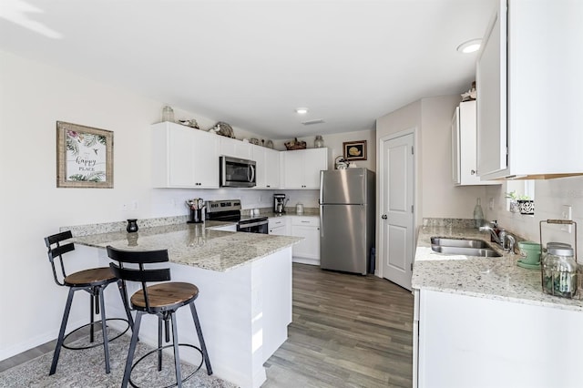 kitchen featuring hardwood / wood-style flooring, appliances with stainless steel finishes, light stone countertops, sink, and a kitchen bar