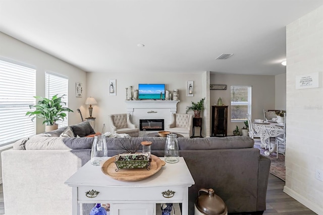 living room featuring dark wood-type flooring, a large fireplace, and brick wall