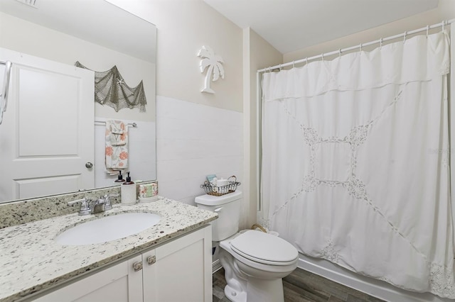 full bath with toilet, wainscoting, tile walls, and vanity