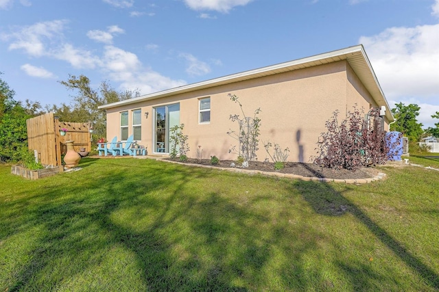 rear view of house featuring a lawn and stucco siding