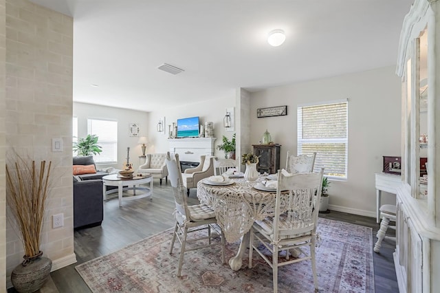 dining space featuring a fireplace, dark wood-type flooring, and plenty of natural light