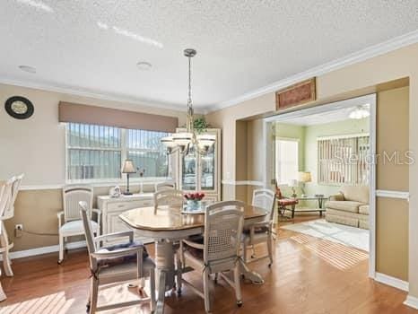 dining space featuring a textured ceiling, a notable chandelier, ornamental molding, and hardwood / wood-style flooring