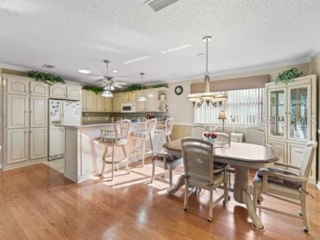 dining space with crown molding, light wood-type flooring, ceiling fan with notable chandelier, and a textured ceiling