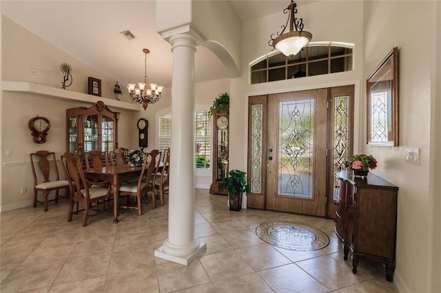 tiled entryway featuring a healthy amount of sunlight, high vaulted ceiling, ornate columns, and an inviting chandelier