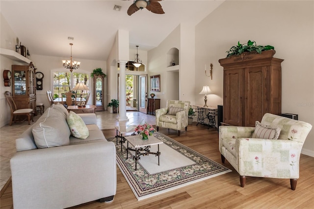 living room featuring ornate columns, ceiling fan with notable chandelier, and light wood-type flooring