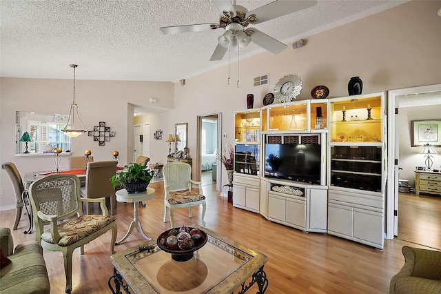 living room featuring a textured ceiling, vaulted ceiling, ceiling fan, and light wood-type flooring