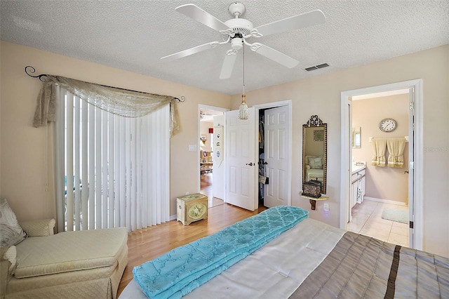 bedroom with ceiling fan, ensuite bathroom, a textured ceiling, a closet, and light wood-type flooring