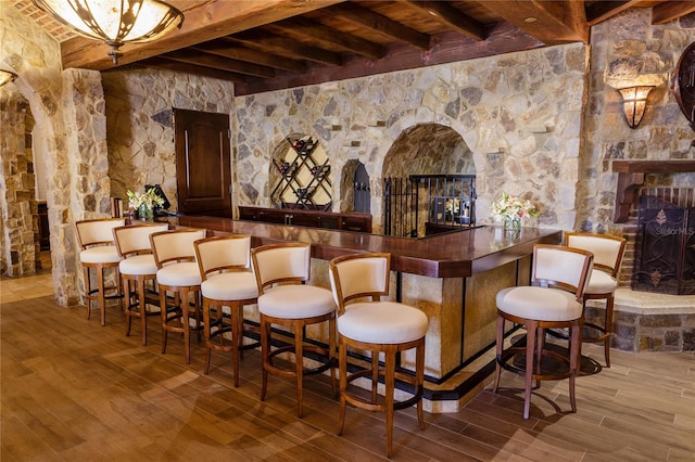 bar with a stone fireplace, hardwood / wood-style flooring, and beamed ceiling