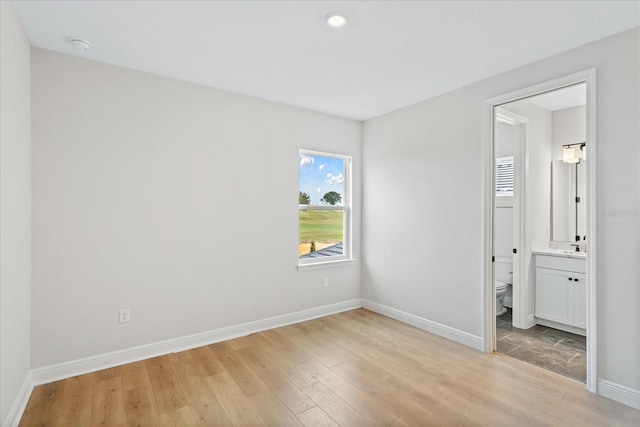 unfurnished bedroom with ensuite bathroom and light hardwood / wood-style flooring