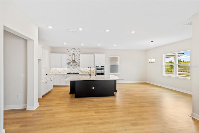 kitchen with a chandelier, light wood-style flooring, white cabinets, backsplash, and an island with sink