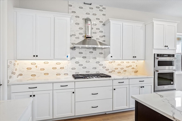 kitchen with white cabinetry, light wood-type flooring, appliances with stainless steel finishes, wall chimney exhaust hood, and tasteful backsplash