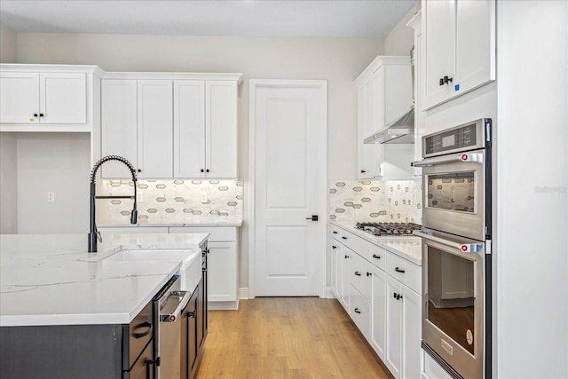 kitchen featuring light stone countertops, light wood-type flooring, backsplash, white cabinetry, and appliances with stainless steel finishes