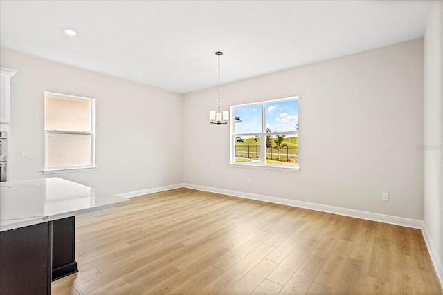 unfurnished dining area with light wood-style floors, a notable chandelier, and baseboards