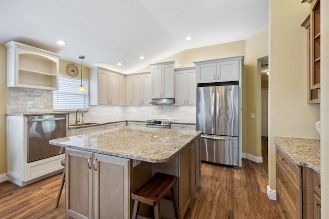 kitchen with lofted ceiling, sink, appliances with stainless steel finishes, a kitchen island, and a kitchen bar