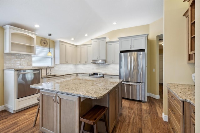 kitchen with a kitchen bar, appliances with stainless steel finishes, sink, light stone counters, and a center island