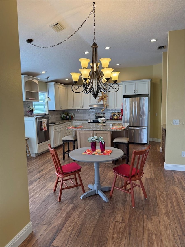 dining space featuring sink, dark wood-type flooring, a textured ceiling, and a notable chandelier