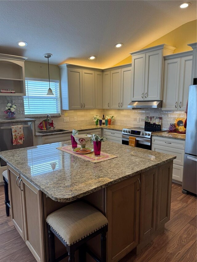 kitchen with appliances with stainless steel finishes, a kitchen breakfast bar, dark wood-type flooring, decorative light fixtures, and a center island