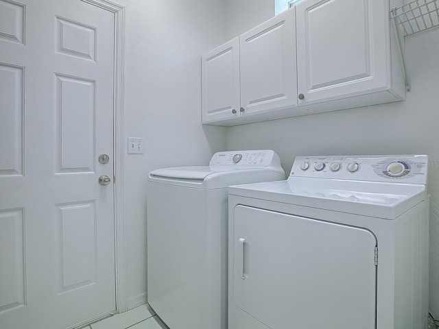 clothes washing area with washer and clothes dryer, cabinets, and light tile floors