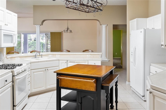 kitchen featuring white appliances, decorative columns, white cabinetry, and sink