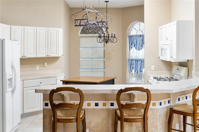 kitchen featuring white cabinets, a kitchen bar, white appliances, and an inviting chandelier